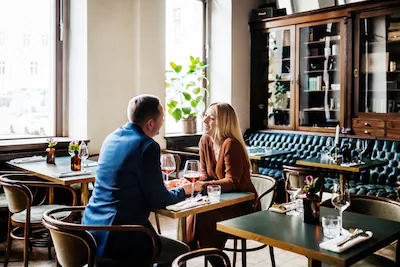 a-couple-holding-hands-while-sitting-down-at-a-table-and-drinking-red-wine-in-a-restaurant-for-lunch.webp