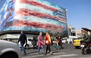 epa12775532-iranians-walk-next-to-a-huge-anti-u-s-billboard-on-a-street-in-tehran-iran-25-february-2.webp