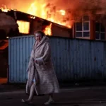 a-woman-walks-past-a-burning-house-at-the-site-of-russian-missile-and-drone-strike-amid-russia-s-att.webp