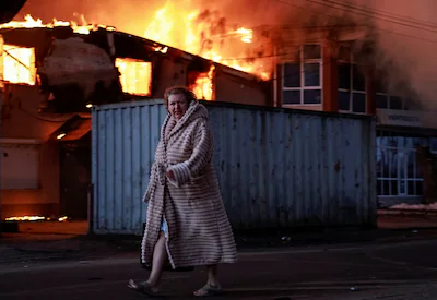a-woman-walks-past-a-burning-house-at-the-site-of-russian-missile-and-drone-strike-amid-russia-s-att.webp