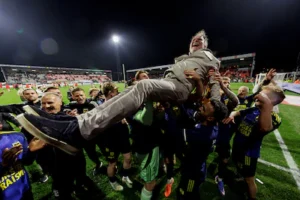 henk-de-jong-op-de-schouders-van-zijn-spelers-na-behalen-promotie.webp