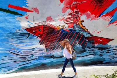 1781311623_a-woman-walks-past-an-anti-us-and-anti-israel-mural-depicting-missiles-hitting-an-aircraft-carrier-i.jpeg