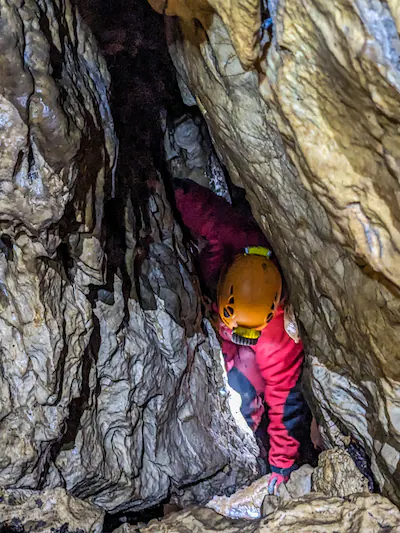 caver-squeezing-through-a-tight-limestone-passage-in-a-narrow-cave-entrance-nera-gorge-beusnita-nati.webp