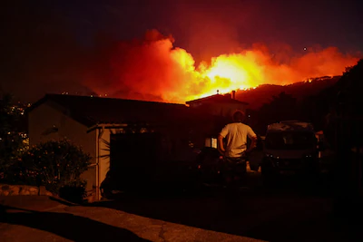 a-person-looks-on-as-flames-and-smoke-from-a-wildfire-rise-near-calonge-spain-july-3-2026-reuters-br.webp